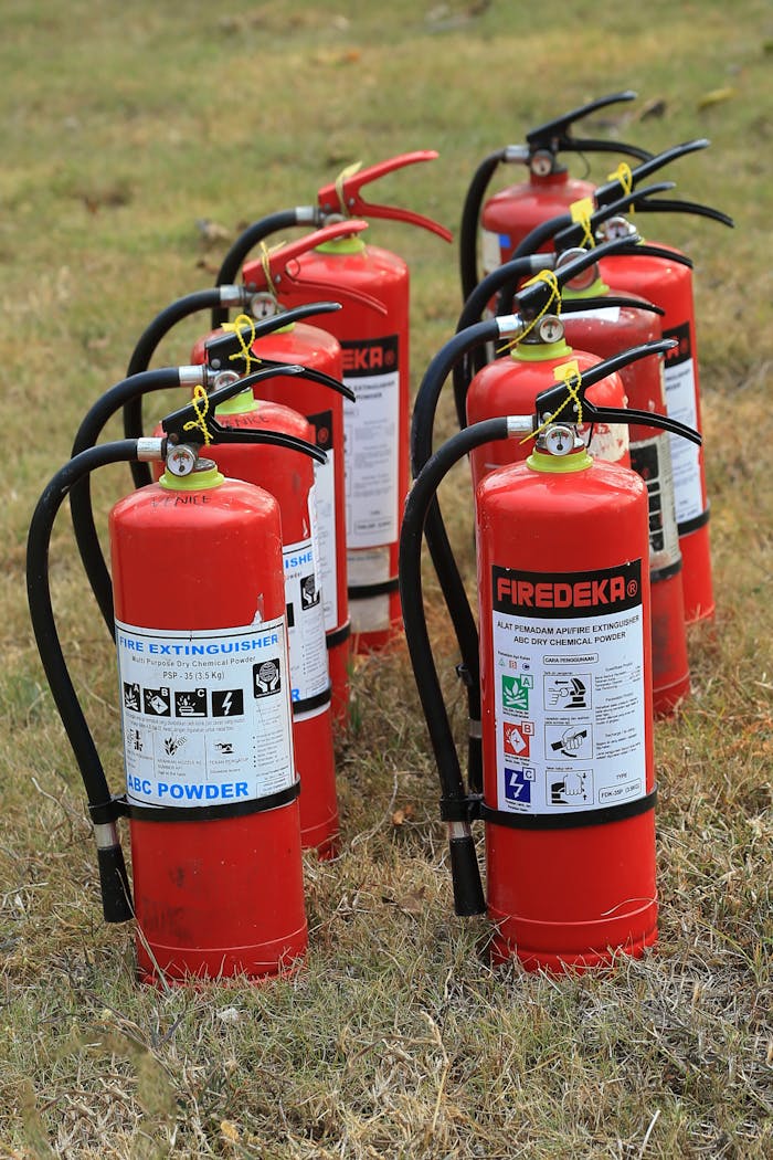 Multiple fire extinguishers lined up on grass, ready for emergency use, showcasing fire safety equipment.