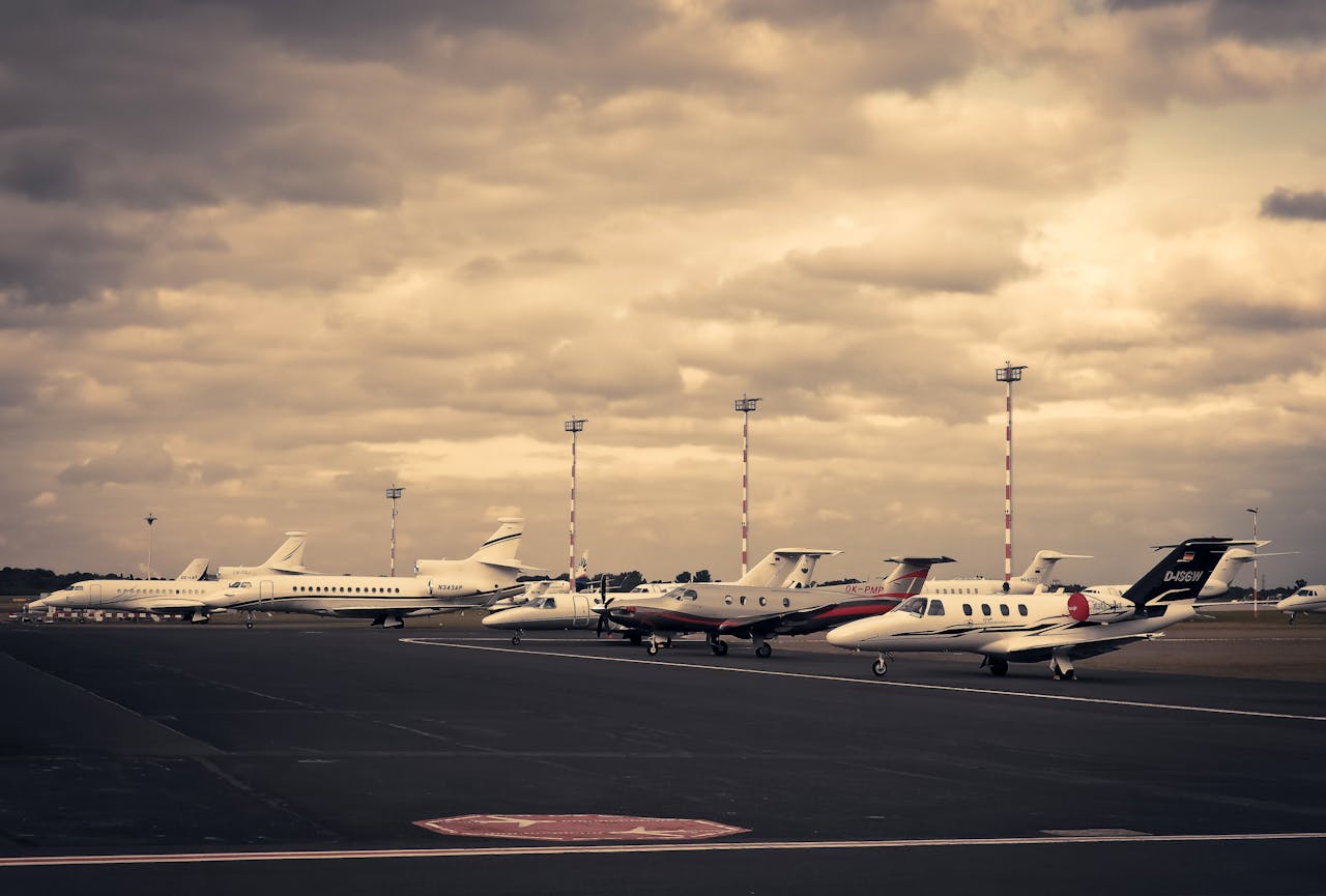 about-img-01 Line of private jets parked on the tarmac under a dramatic cloudy sky, showcasing aviation and travel.