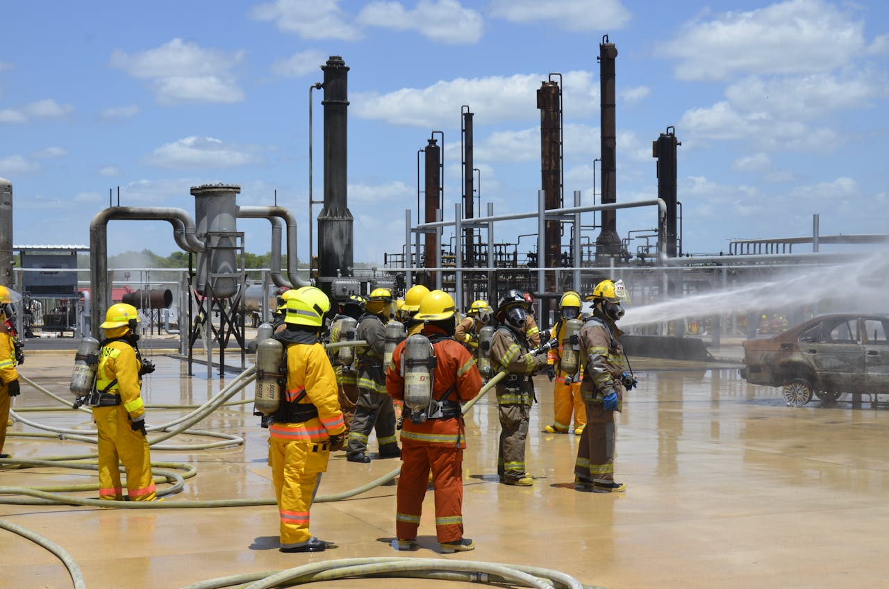 home-img Firefighters wearing protective gear conduct a safety drill at an industrial site with heavy equipment.